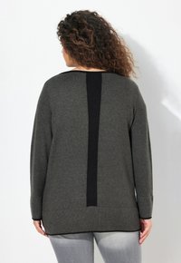Pull gris foncé avec un panneau vertical noir côtelé dans le dos, des manches longues et une coupe décontractée avec des poignets et un ourlet côtelés.