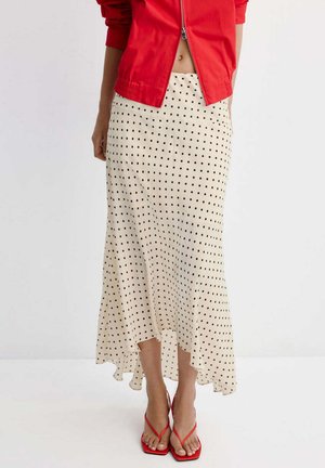 Falda midi blanca con lunares negros, combinada con una chaqueta roja con cremallera y tacones rojos de tiras con punta cuadrada.