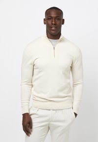 Cremefarbener Reißverschlusspullover aus weichem Strickstoff, mit hohem Kragen, langen Ärmeln und gerippten Bündchen und Saum.