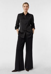 Black satin blouse with a button-down front, long sleeves, and a pointed collar, paired with wide-leg black trousers and dark footwear.
