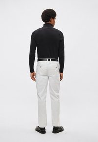 Czarna koszula z długim rękawem, białe, dopasowane spodnie noszone z czarnym paskiem. Gładka tekstura i dopasowany krój, widok od tyłu.