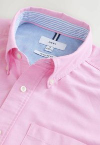 Camisa de botón rosa claro con un cuello interior a rayas azules, botones blancos, bolsillo frontal y etiquetas de tamaño dentro del cuello.