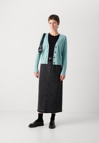 Light blue cardigan with buttons over a black top, paired with a dark denim maxi skirt and black shoes. Smooth textures and layered design.