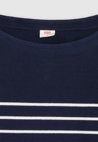 T-paita tummansinistä, pyöreällä kaula-aukolla, jossa on kolme vaakasuoraa valkoista raitaa keskellä. Pehmeää kangasta tasaisella pinnalla.