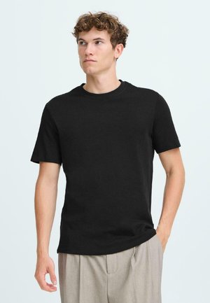 Black short-sleeve t-shirt with a crew neckline, made of a smooth fabric, paired with light gray pleated trousers. Simple design, no patterns.