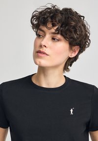 T-shirt nera in cotone con scollo rotondo e maniche corte. Presenta un piccolo logo bianco nella zona sinistra del petto. Tessuto liscio.