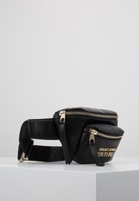 Černá kožená ledvinka se dvěma zipovými kapsami, zlatými zipy a zlatým logem "Versace Jeans Couture" na přední kapse.