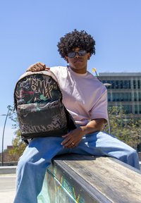 Mochila con un diseño gráfico que presenta a un ciclista de BMX, predominantemente negra con acentos coloridos, fabricada con material duradero y de forma rectangular.