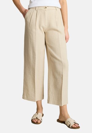 Beige strukturierte, weit geschnittene, gekürzte Hose mit vorderen Falten, getragen mit einem weißen Top und cremefarbenen Slip-on-Sandalen an einem Model.