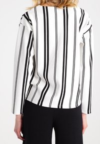 Vit långärmad skjorta med vertikala svarta ränder, i avslappnad passform och med rundad halsringning. Slätt, strukturerat tyg.