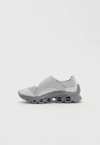 Scarpa sportiva grigia con tomaia in mesh e suede, dotata di suola imbottita e distintivi dettagli perforati lungo i lati.