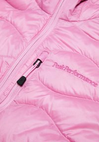 Giacca trapuntata rosa con zip e logo Peak Performance. Presenta una texture liscia e lucida e dettagli di cucitura ben definiti.