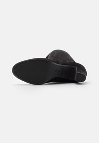 Stivale in suede nero al ginocchio con punta rotonda e tacco sottile e allungato. La suola è liscia e piatta, con dettagli di branding discreti vicino al tallone.