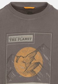 Graues Baumwoll-T-Shirt mit einem grafischen Druck von Bergen und einer großen orangefarbenen Sonne. Rippenkragen mit einem kontrastierenden orangenen Etikett.