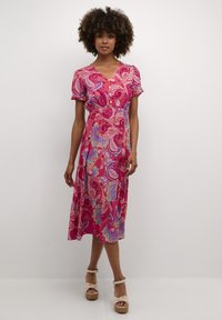 Robe midi rose à motif cachemire avec des manches courtes bouffantes, décolleté en V et détails de boutons. Fabriquée en tissu léger avec une coupe fluide.