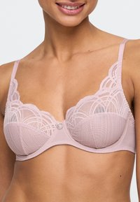 Jasnoróżowy stanik koronkowy z fiszbinami, przezroczystymi miseczkami, falbany na krawędziach i centralnym dekoracyjnym pierścieniem. Regulowane ramiączka zapewniają wsparcie.