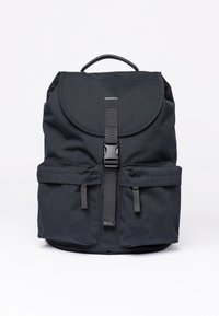Zaino in tessuto nero con flap arrotondato, strap regolabile, tasche frontali e manico superiore. Presenta una texture liscia e un branding minimo.
