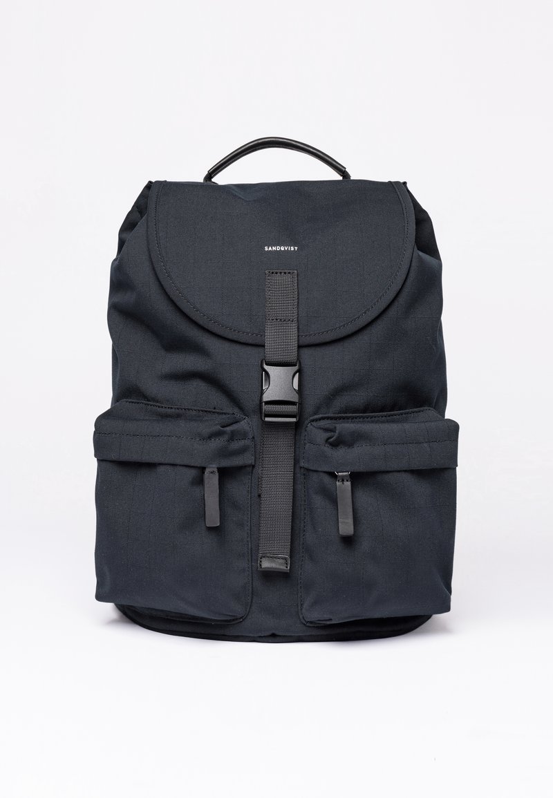 Zaino in tessuto nero con flap arrotondato, strap regolabile, tasche frontali e manico superiore. Presenta una texture liscia e un branding minimo.