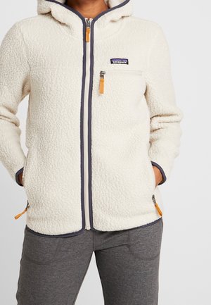 Weißer Fleece-Zip-Up mit Kapuze, Reißverschlusstasche auf der Brust und Seitentaschen, getragen mit grauer Hose, mit Patagonia-Logo auf der Brust.