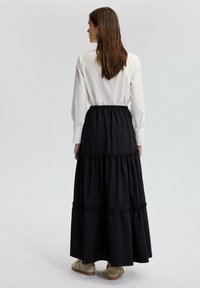 Zwarte, gelaagde maxi-jurk met gerimpelde rand, gecombineerd met een witte blouse en lichte schoenen. Focus op een eenvoudig en casual ontwerp.