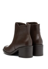 Botine din piele maro, cu un finisaj neted, vârf rotunjit și toc pătrat. Interiorul este căptușit cu un material moale. Design simplu, fără accesorii.