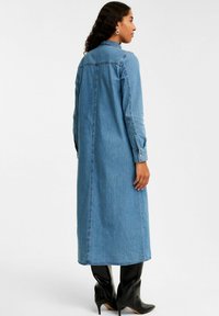 Denimskjortklänning i ljusblått, med långa ärmar, krage och rak passform. Matchad med knähöga svarta stövlar med klack.