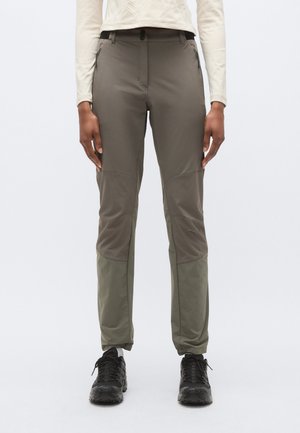 Technické vonkajšie nohavice v dvoch odtieňoch olivovej zelenej, s pružnou látkou, vreckami na zips a zosilnenými panelmi na kolenách, doplnené o čiernu obuv.