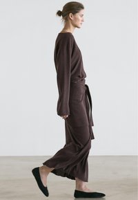 Brown knit loungewear set featuring a long-sleeve top and wrap-around skirt with a tie, paired with black flat shoes. Simple and flowing design.