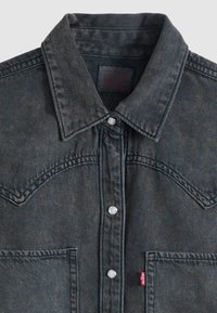 Σκούρο γκρι μπουφάν από τζιν ύφασμα με μυτερό γιακά, κουμπιά τύπου «snap», μπροστινές τσέπες και μια μικρή κόκκινη ετικέτα Levi’s στην αριστερή τσέπη.