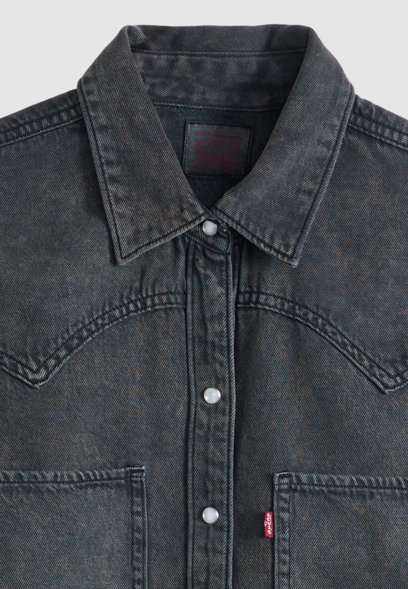 Dark gray denim jacket with pointed collar, snap buttons, front pockets, and a small red Levi’s tag on the left pocket.