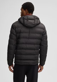 Giacca imbottita nera con cappuccio, design trapuntato, polsini elastici e una texture leggermente lucida, vista da dietro.