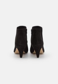 Stivaletti in suede neri con tacco conico, cerniere laterali e una superficie liscia e opaca. Presentano una punta arrotondata e una suola beige.
