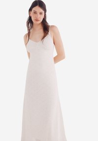 Robe longue blanche sans manches avec un décolleté arrondi, présentant un motif géométrique texturé et une silhouette fluide.