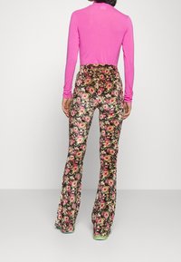 Zúžené květinové kalhoty s černým pozadím, zdobené růžovými a žlutými květy. Vyrobeno z hladké tkaniny, s vysokým pasem.