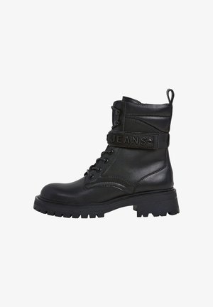 Mustat nahkaiset nilkkurisaappaat pyöreällä kärjellä, nauhakiinnityksellä ja kumipohjalla. Nilkan ympärillä on "JEANS"-niminen remmi.