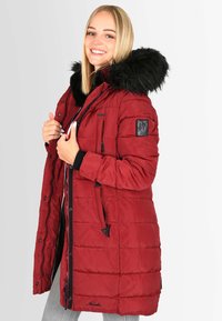Red puffer jacket with a fur-lined hood, quilted design, front pockets, and black accents. Zipper and button closures.