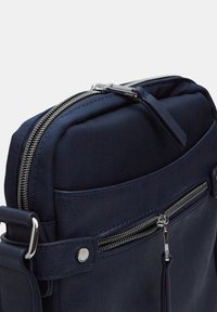 Marineblauwe leren tas met textiel, voorzien van dubbele zilveren ritssluitingen, een voorvak met rits en een verstelbare schouderband. Glad finish, compact ontwerp.
