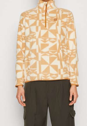 Pull polaire beige et blanc à motifs géométriques avec fermeture éclair au quart, porté avec un pantalon vert olive foncé à poches latérales.