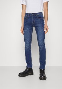 Mörkblå jeans i denim med smal passform, femfickorsdesign, subtila söm detaljer, bärs med svarta ankelstövlar.