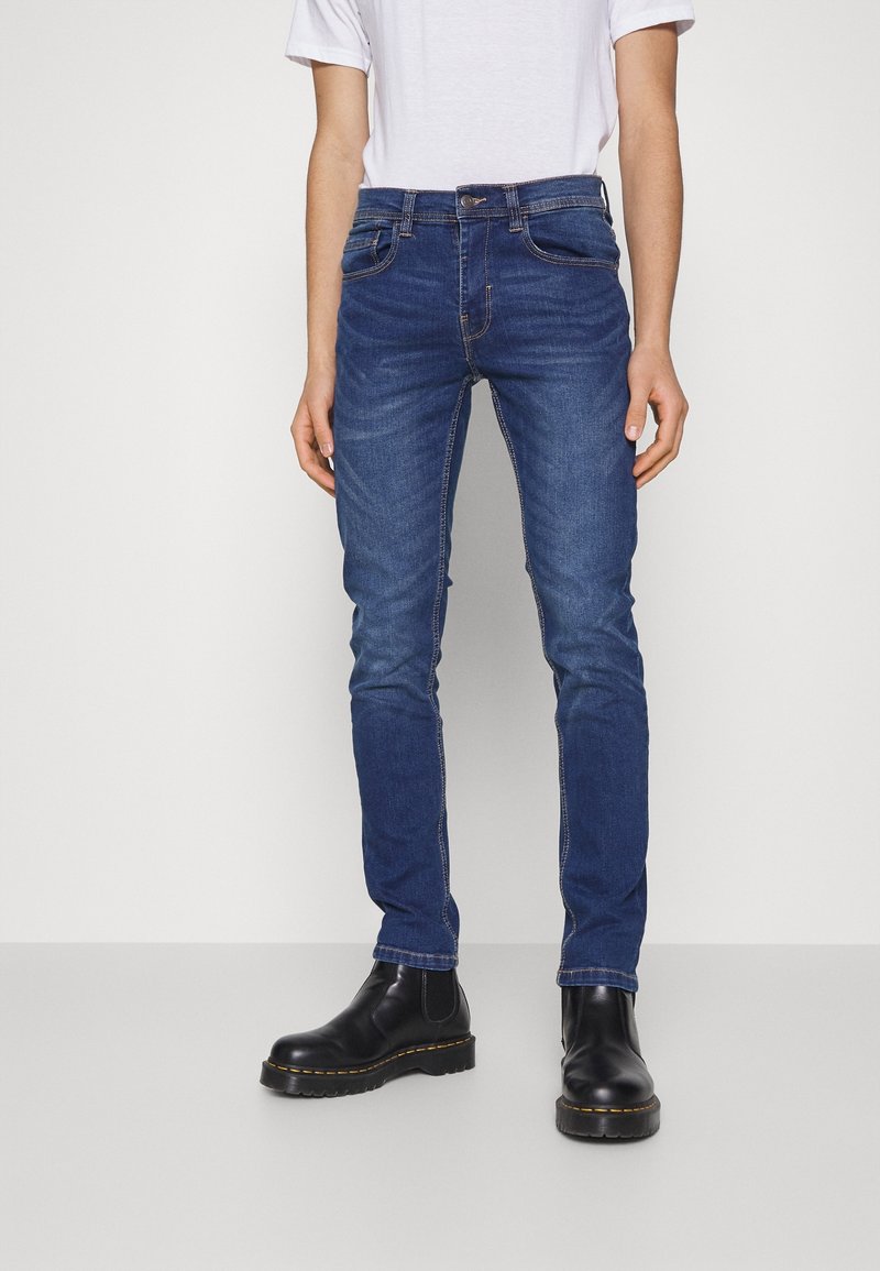 Mörkblå jeans i denim med smal passform, femfickorsdesign, subtila söm detaljer, bärs med svarta ankelstövlar.