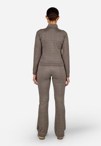 Ruda raukšlėta megzta palaidinė su aukštu apykaklė ir derančiomis platėjančiomis kelnėmis. Medžiaga turi subtilią tekstūrą, pabrėžiančią komfortą ir prigludimą.