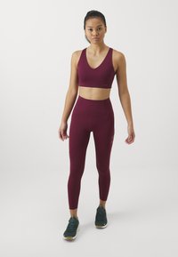Bordó sportmelltartó és magasan derekú leggings rugalmas anyagból, minimalista dizájnnal és diszkrét oldalzsebekkel.