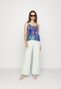 Top de alças com padrão floral em azul, rosa e verde, combinado com calças largas verde claro e sandálias brancas.