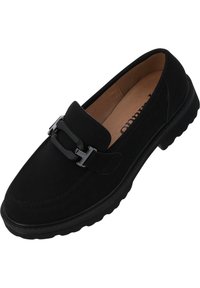 Scarpa nera in suede, slip-on, con punta arrotondata, caratterizzata da un'accento in metallo a forma di fibbia e una suola in gomma testurizzata. L'interno è di colore beige.