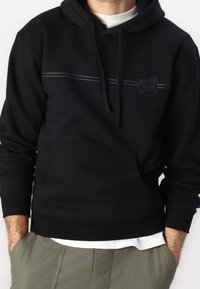 Svart huvtröja med kanguruficka, med en texturerad logotyp och en horisontell grå rand över bröstet.