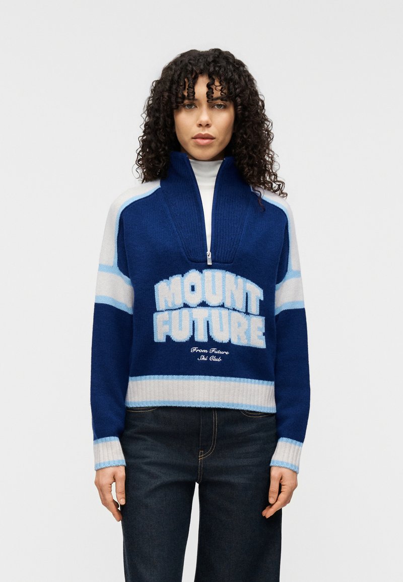 Μπλε πλεκτό πουλόβερ με ψηλό γιακά και κλείσιμο με φερμουάρ. Διαθέτει τη φράση "MOUNT FUTURE" σε λευκά και ανοιχτά μπλε γράμματα, καθώς και αντίθετες ρίγες.