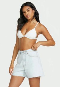 Top de bikini triângulo branco combinado com calções de ganga de cintura alta azul claro; os calções apresentam uma bainha desfeita e bolsos frontais.