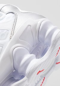 Gros plan de la semelle blanche d'une chaussure de sport avec des coussinets amortissants à motif tourbillonnant et un grip texturé avec des accents rouges.