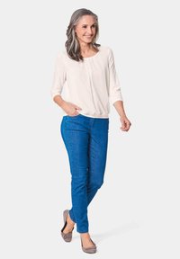 Helle Bluse mit drei Viertelärmeln, kombiniert mit blauen Slim-Fit-Jeans. Graue Ballerinas mit einer Schleife runden das Outfit ab.