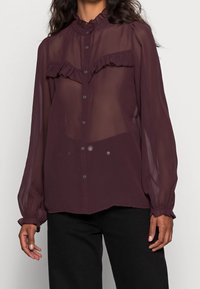 Gennemsigtig burgunderrød bluse med en flæsekrave og frontpanel; fulde ærmer med elastiske manchetter; diskrete knapdetaljer foran.